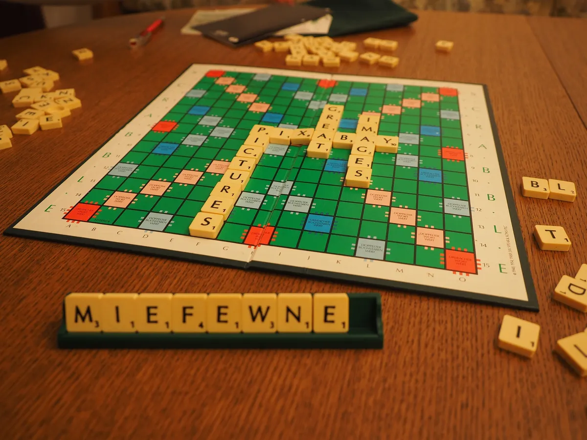 A Scrabble board on a table. Some tiles have been played on the board and other tiles are to the side, waiting to be played.