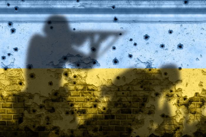 A silouette of soldiers fighting on a wall painted in the colors of the Ukrainian flag