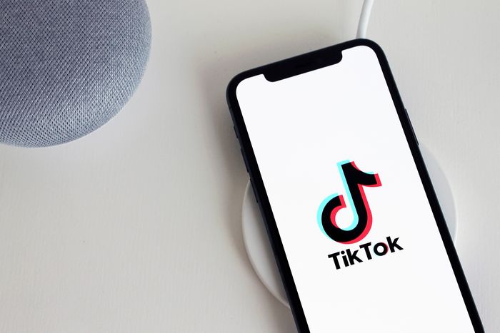 A phone on a charger next to a speaker. The TikTok logo is on the screen of the phone.