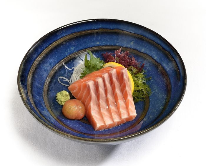 A small round plate with salmon sashimi, some salad, and a dab of wasabi.