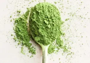 Green powdered matcha tea on a teaspoon and spilling over the sides onto a white background.