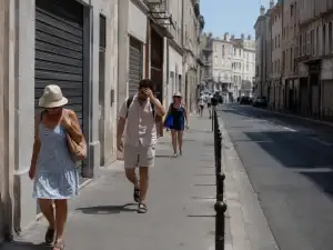 A quiet French city street during a severe heat wave, with closed shop shutters, pale buildings, hard sunlight, and a few people walking slowly in summer clothes.