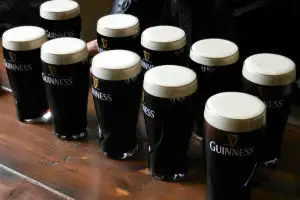 Several pints of Guinness with thick white foam sit on a wooden bar.