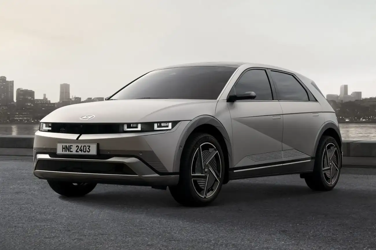 A silver Hyundai Ioniq 5 parked beside a river, shown from the front and side with a city skyline in the background.