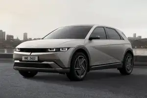 A silver Hyundai Ioniq 5 parked beside a river, shown from the front and side with a city skyline in the background.