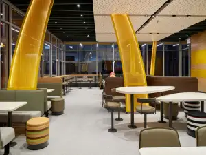 Empty modern fast-food restaurant dining area with large yellow curved columns, booths, tables, and stools.