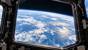 Earth’s blue ocean, white clouds, and curved horizon seen through a large spacecraft window.